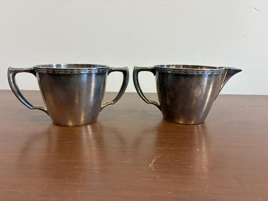 Silverplate sugar bowl and creamer with handles on a wooden surface.