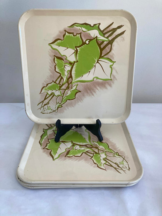 Stack of six vintage cream metal trays with green ivy leaf botanical design, one tray displayed upright on a stand.