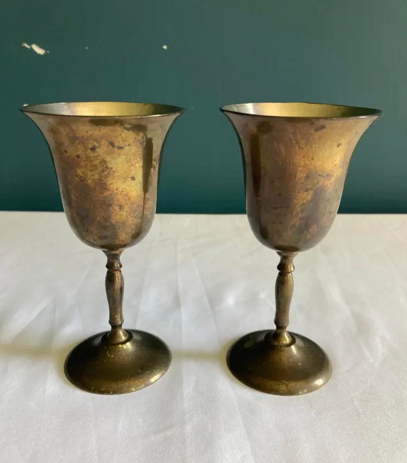 Two brass goblets on a white surface with a dark green background