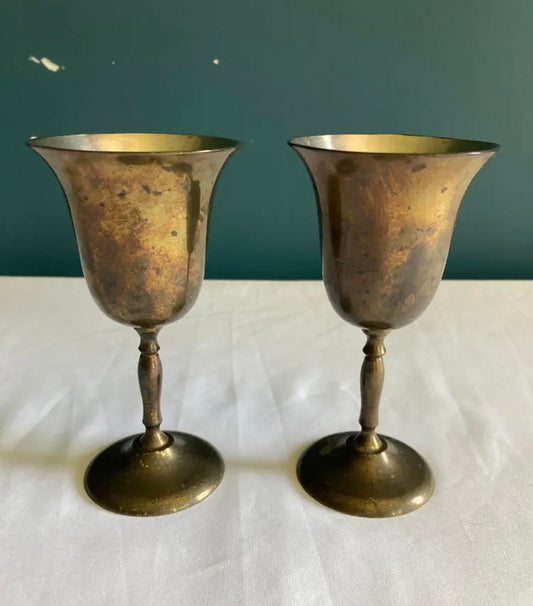 Two brass goblets on a white surface with a dark green background