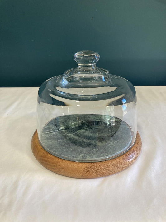 Vintage Cornwall USA cheese tray with clear glass dome lid, round teak wood and green marble base, and compact size for serving or display. Cheese tray is sitting on a white cloth in front of a teal background.