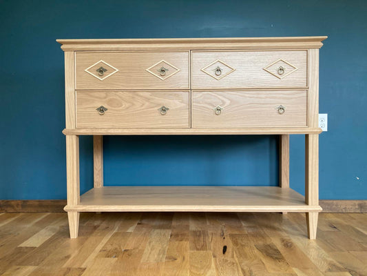 Wooden dresser with four drawers and a bottom shelf sitting against a blue wall.