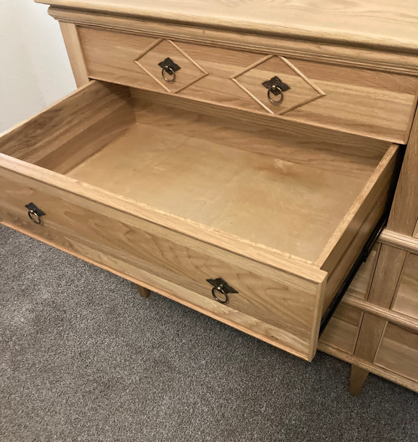  A light wood dresser with drawers. The top drawer is closed and the 2nd drawer is open. The drawers have ornate metal handles. The dresser is sitting on a light brown carpet.