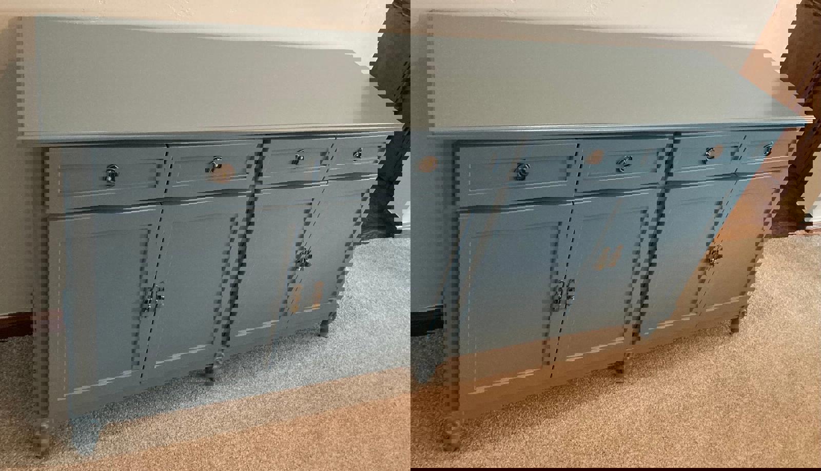  A light blue wooden cabinet with four doors and four drawers. The cabinet has brass knobs and is sitting on a light brown carpet.