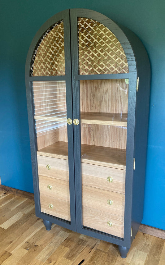 Hand Crafted of solid oak by JC Furniture in Oklahoma City. This beautiful arched cabinet features bent wood, brass handles and hinges, and glass, wood, and brass mesh doors. The three drawers are made with dovetails and are very sturdy. The feet have been hand turned on a lathe.  It is finished with Sherwin Williams Iron Ore colored paint on the outside and left the natural wood on the inside.