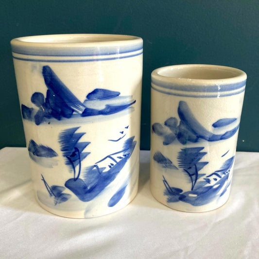 Two ceramic cups with blue fish patterns on a white surface against a dark green background