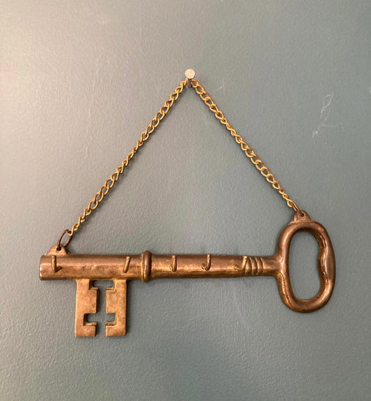 Decorative brass key with five hooks and a chain on a plain wall