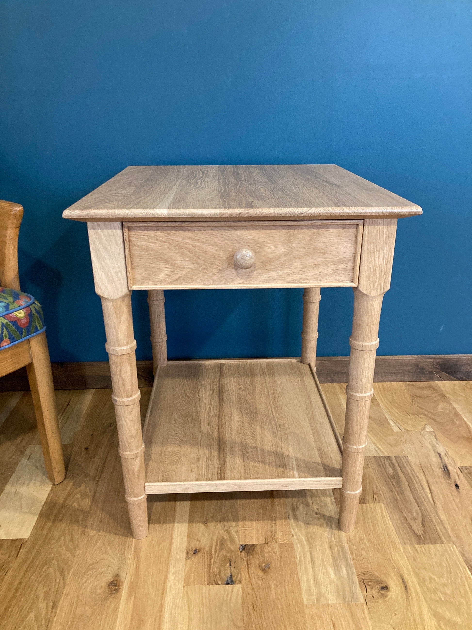  A light solid wood end table with a single drawer and a lower shelf. The table has turned faux bamboo legs and a simple design.
