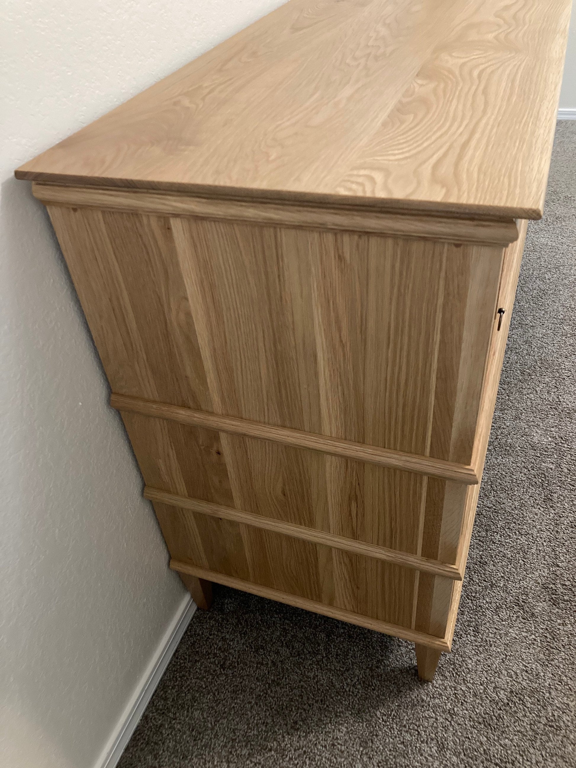 A light wood dresser with eight drawers and a top shelf. The dresser has a simple design with a smooth surface and a light wood finish.
