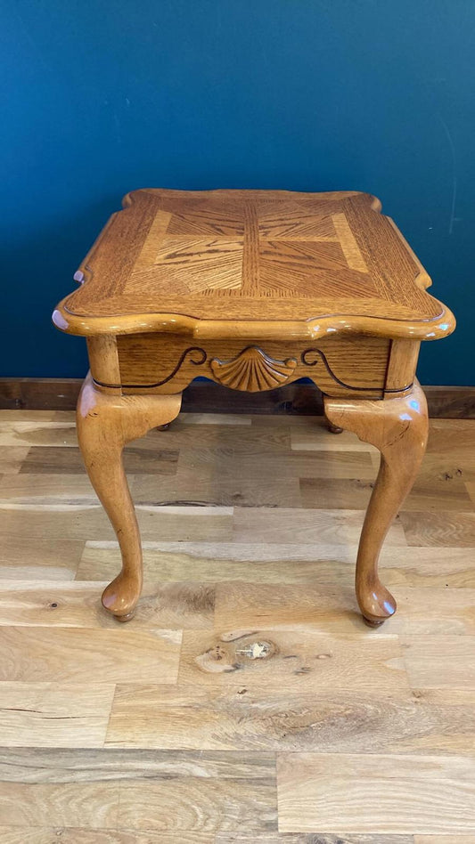 A light oak wood end table with cabriole legs and a rectangular top. The top features an inlaid parquetry design. The table has carved shell details on the apron. This classic style accent table is perfect for a living room or bedroom.