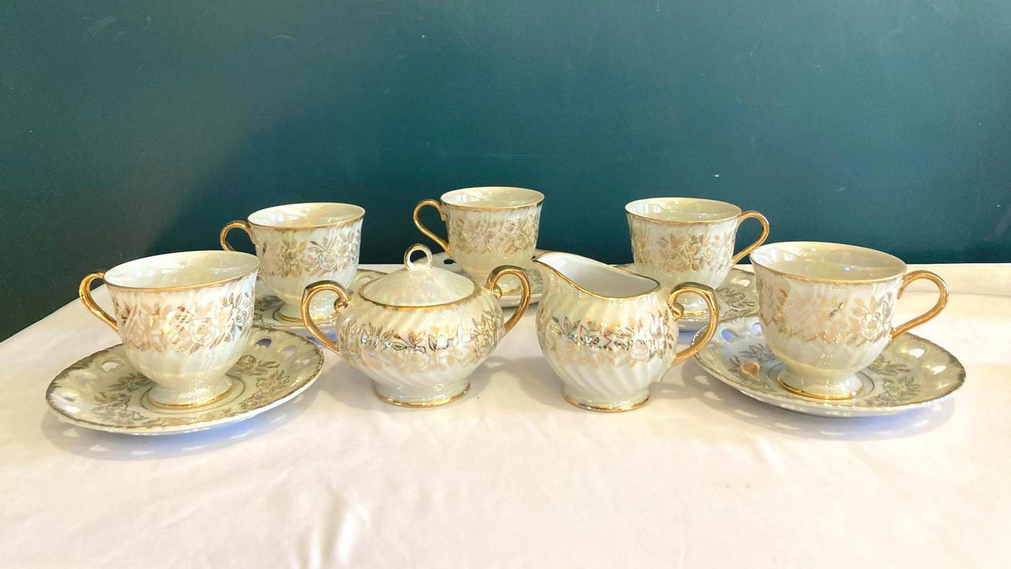 Set of ceramic tea cups and saucers with gold detailing on a white surface against a teal background.