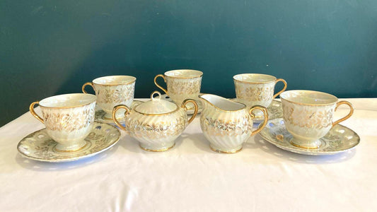 Set of ceramic tea cups and saucers with gold detailing on a white surface against a teal background.