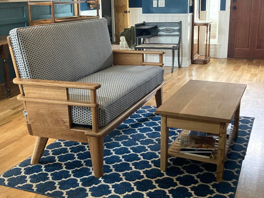 Handmade oak couch with a modern open-arm frame design, upholstered in blue and white houndstooth-style fabric, positioned on a blue rug on a wood floor next to a paneled wall.