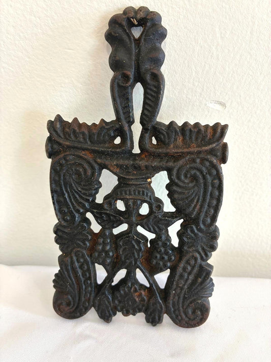 Decorative black metal wall hanging trivet with intricate designs on a white background
