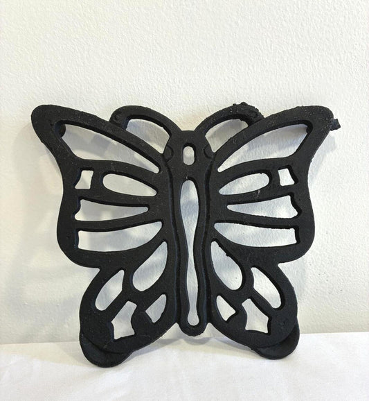 Vintage black cast iron butterfly trivet with openwork wing design for kitchen or decorative use.